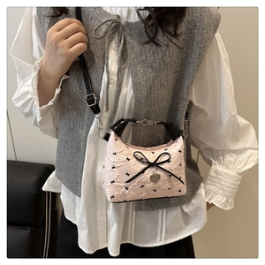 Detail of pink bow handbag with heart charm and textured fabric on casual outfit