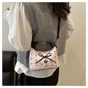 Close-up of pink quilted shoulder bag featuring black bow detail and heart pendant