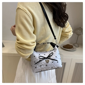 Detailed side view of white quilted shoulder bag with black bows and heart charm decoration
