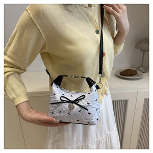 Detail of white wrinkled mini bag with black bow prints and heart charm on a model