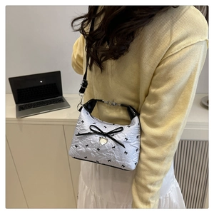 Detailed shot of white floral shoulder bag with black bow and gold heart pendant