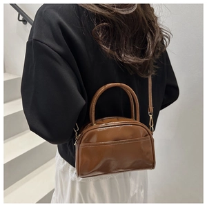 Detail of brown patent leather mini handbag with gold hardware and adjustable strap