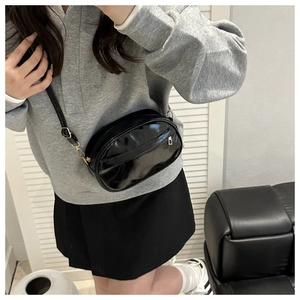 Detail of glossy black oval crossbody bag with gold-tone hardware and adjustable strap