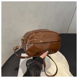 Detailed macro view of the brown patent leather finish and gold metal chain on the bag