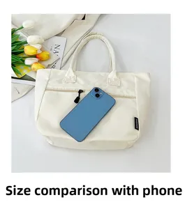 Macro shot of off-white nylon tote bag with front zipper pocket and size comparison to phone