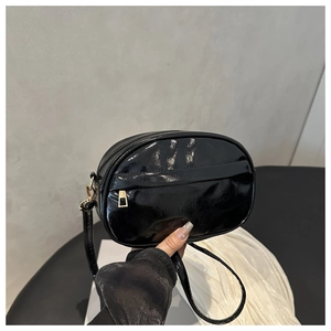 Close-up of glossy black crossbody bag with gold zipper and adjustable shoulder strap