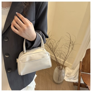Detail of a creamy white mini Boston bag featuring smooth leather texture and front pocket