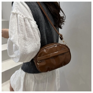 Side view of a brown glossy leather crossbody shell bag worn by a model in casual attire