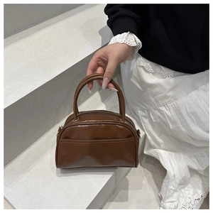 Detail of a brown glossy leather bowling bag with top handles on a grey stone step