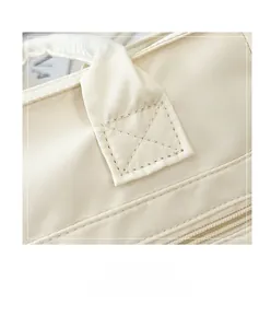 Close-up of reinforced X-shaped stitching on cream canvas tote with zipper detail
