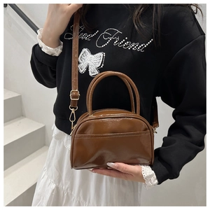 Sac à main marron brillant porté en bandoulière par un mannequin sur escalier blanc