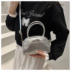 Détail d'un sac à main semi-circulaire argenté avec bandoulière amovible et poignée rigide