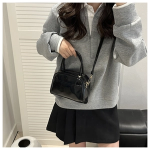 Detailed view of a black patent leather Boston handbag with twin handles and shoulder strap