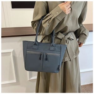 Detail of blue nylon tote bag showing dual vertical zipper pockets and long straps
