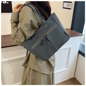 Detail of dark grey nylon tote bag showing double zip pockets and a shoulder strap