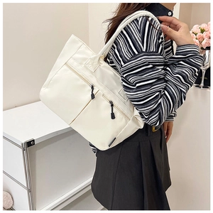 Detail of white nylon tote bag with functional zipper pockets and reinforced handles