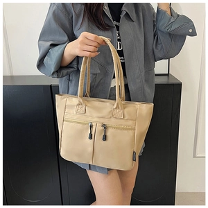 Detail of beige nylon tote bag featuring vertical zipper pockets and a logo label