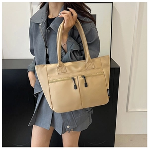 Detail view of beige nylon tote bag with dual horizontal zipper pockets and fashion tag