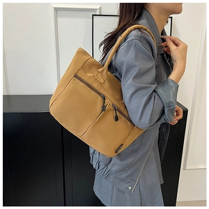 Detail of mustard nylon tote bag with dual zipper pockets and fashion label on shoulder