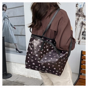 Close-up of black tote bag featuring pink floral print and white bow patterns with long straps