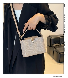 Detail of silver sequined handbag featuring a V-shaped metal clasp and sleek top handle