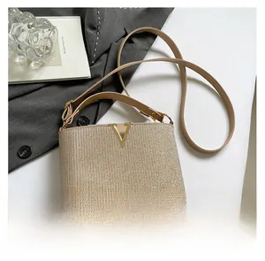 Detail of champagne woven texture handbag featuring a gold V-shaped buckle closure