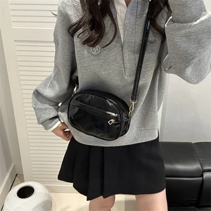 Minimalist black patent leather crossbody bag with adjustable strap worn by a model