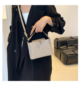 Detail of glittery champagne gold handbag featuring a gold V buckle and textured finish