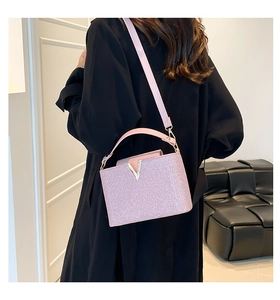 Pink sequin shoulder bag with golden V-shaped buckle worn by a model in black clothing