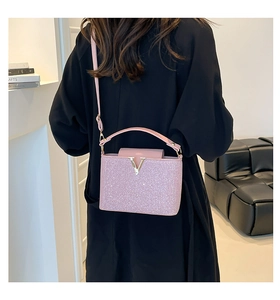 Sac bandoulière rose à paillettes avec logo V doré porté par un mannequin en intérieur
