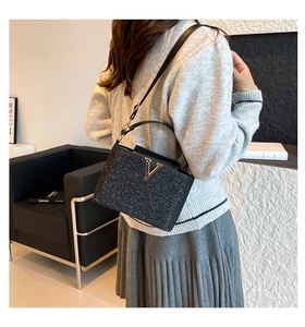 Detail of black sequined handbag featuring a gold V-shaped buckle and textured surface