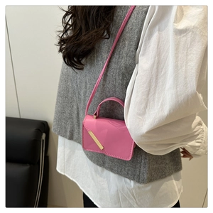 Sac à main rose en cuir avec garniture dorée et poignée porté par un mannequin féminin