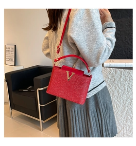 Close-up of a red glittery mini crossbody bag featuring a golden V-shaped metallic logo