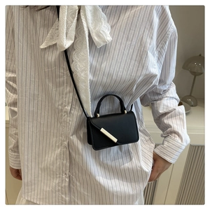 Close-up of minimalist black leather crossbody bag with elegant gold metal buckle detail