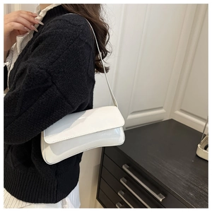 Detail of white glossy baguette bag with flap closure worn as a minimalist shoulder bag