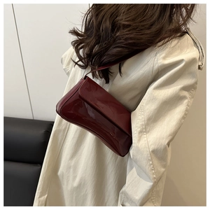 Glossy burgundy PU leather crossbody bag worn as a shoulder bag with chic trench coat