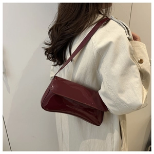 Detail of glossy wine red patent leather shoulder bag worn with a beige trench coat