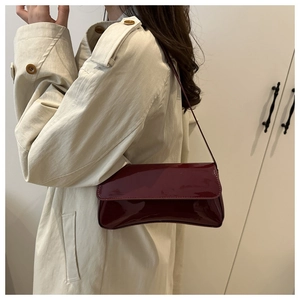 Détail d'un sac sous le bras en cuir verni bordeaux porté par un mannequin en manteau