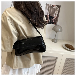 Side view of black glossy patent leather baguette bag worn by a model in a minimalist room