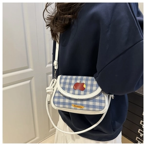 Detail of blue and white checkered crossbody bag with red apple patch and thin white strap