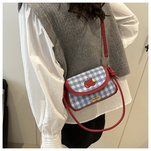 Detail of blue and white checkered crossbody bag with red apple patch and red strap