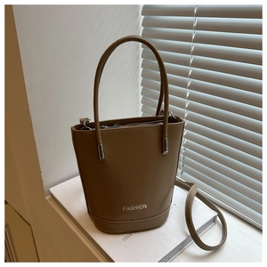 Detail of khaki leather bucket bag with silver zipper and FASHION logo on a windowsill