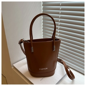 Detail view of brown bucket bag showing the silver fashion logo and metal hardware handles