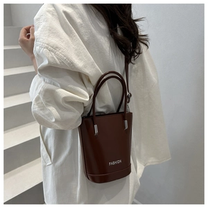 Detail of a brown bucket bag with FASHION logo and adjustable shoulder strap on a model