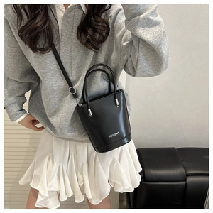 Lifestyle shot of a black glossy bucket bag with FASHION lettering and thin strap