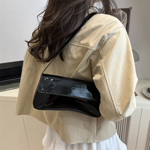 Minimalist black patent leather baguette shoulder bag shown on model in urban office setting
