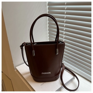 Detail of dark brown bucket bag on books, showing silver hardware and fashion text logo