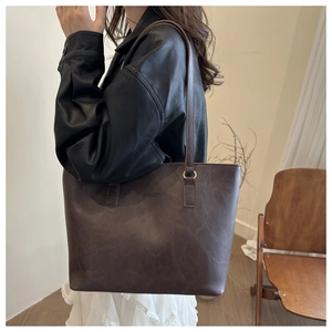 Detail of a dark brown leather tote bag with shoulder straps worn by a model in a minimalist room