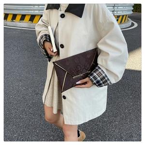 Close-up of brown snake pattern envelope clutch bag with gold metal trim in a street setting