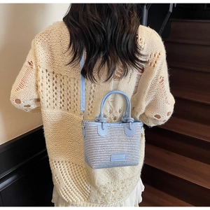 Detail of light blue woven bucket bag with knot handle and adjustable strap worn by model